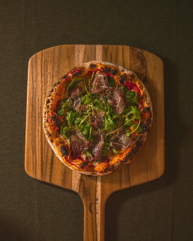 Pizza napolitana com presunto cru e rúcula sobre pá de madeira